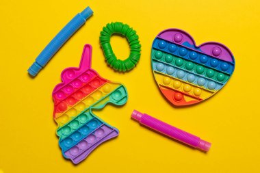 Renkli kırmızı, mavi, pembe, yeşil ve sarı pop tüpü çocuk oyuncakları, tek boynuzlu at ve kalp. Neşeli plastik stres önleyici parlak sarı desenli kağıt arka planda çok renkli oyuncak seti. Düz yatıyordu.