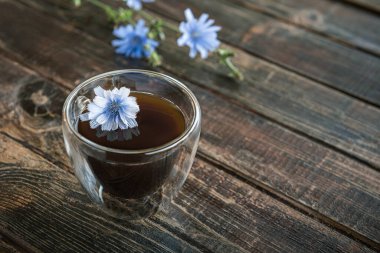 Hindiba, kafeinsiz, termo cam şeffaf bardakta kahveye alternatif kahve, kahverengi doğal ahşap masa üzerinde taze mavi çiçekli hindiba kökleri. Boşluğu kopyala.