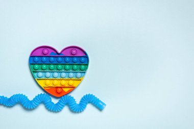 Gökkuşağı kalbi ve gerilmiş, dalga mavi tüp şeklinde bükülmüş. Farklı şekillerde çocuk oyuncakları. Plastik anti-stres oyuncakları mavi kağıt arka planda. Düz yatıyordu. Büyük kopyalama alanı.