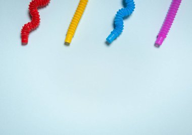Düz ve kıvrımlı dalga şeklinde parlak sarı, kırmızı, pembe ve mavi pop tüplü çocuk oyuncakları. Mavi kağıtta birbirine zıt dört anti-stres oyuncağı. Düz yatıyordu. Büyük kopyalama alanı.