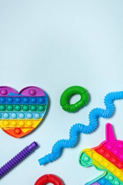 Kırmızı, mor, yeşil ve mavi tüplü çocuk oyuncakları farklı şekillerde dizilmiş, gökkuşağı kalbi ve tek boynuzlu at. Plastik anti-stres oyuncakları mavi kağıt arka planda. Düz yatıyordu. Boşluğu kopyala.