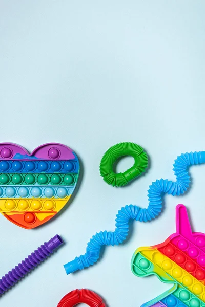 Kırmızı, mor, yeşil ve mavi tüplü çocuk oyuncakları farklı şekillerde dizilmiş, gökkuşağı kalbi ve tek boynuzlu at. Plastik anti-stres oyuncakları mavi kağıt arka planda. Düz yatıyordu. Boşluğu kopyala.