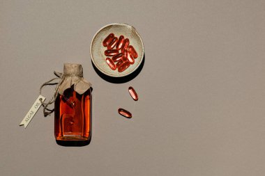 Çamur tabağında alg yağı ve jelatin yağ kapsülleri olan şeffaf bir kap. Cam şişe, ahşap etiketli jüt ipliğiyle bağlanmış. Kahverengi kağıt arka plan. Yenilikçi gıda malzemesi. Boşluğu kopyala.