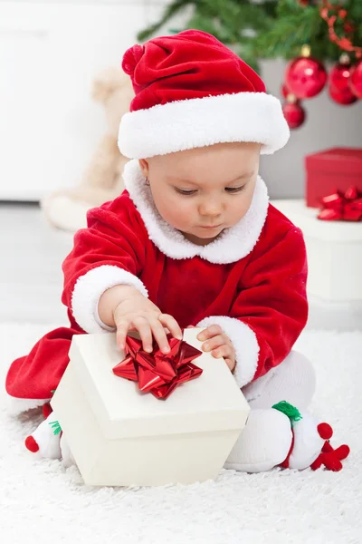 Bébé fille en tenue de père Noël ouvrant un cadeau — Photo