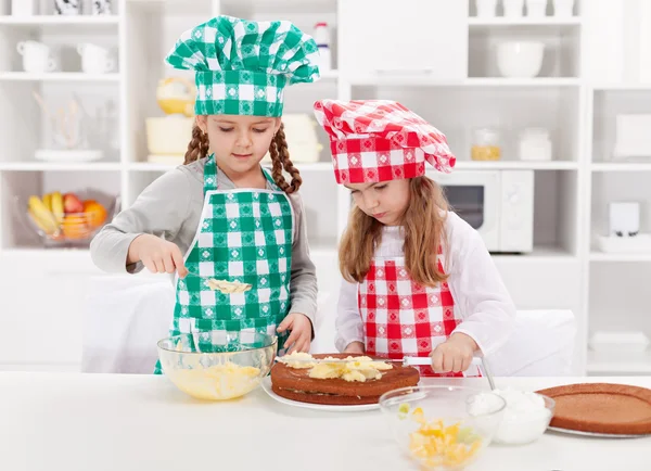 Meninas com chapéus de chef preparando um bolo — Fotografia de Stock