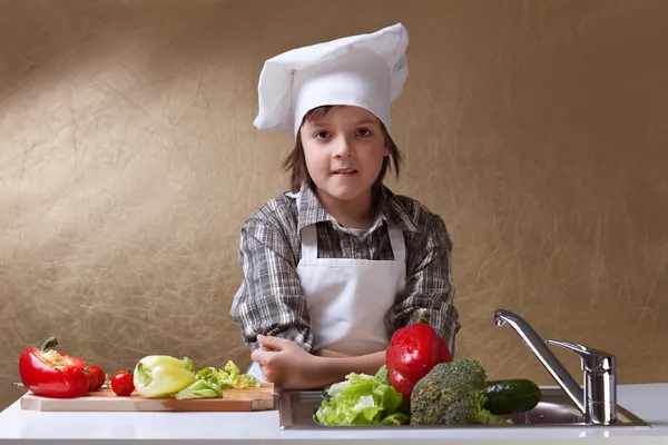 Malý chlapec s klobouku šéfkuchaře mytí zeleniny — Stock fotografie