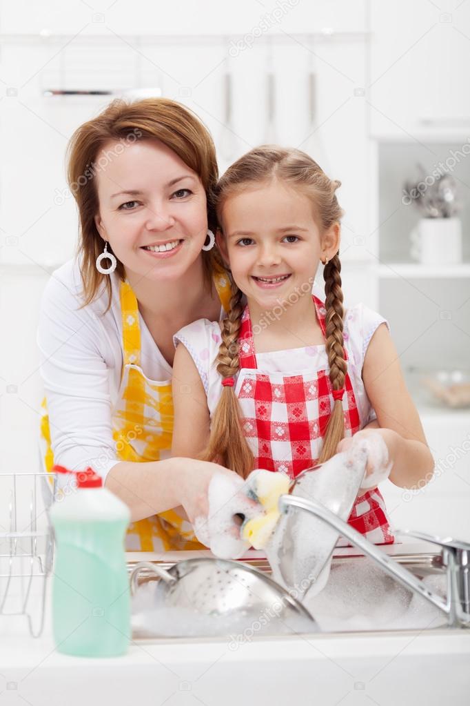 Woman and little girl washing dishes in the kitchen