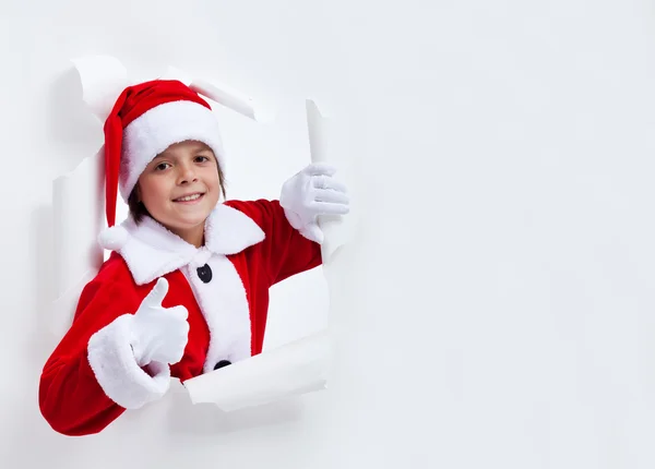 Heureux santa costume garçon penché à travers trou de papier donnant thum — Photo