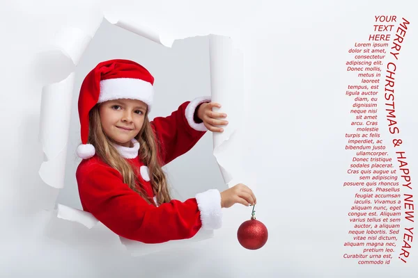 Petite fille en costume de Père Noël penché hors des bords déchirés trou dans p — Photo