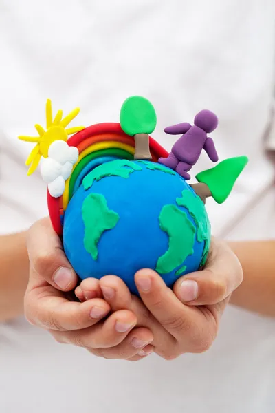 Modelling clay earth with rainbow and trees in child hands — Stock Photo, Image
