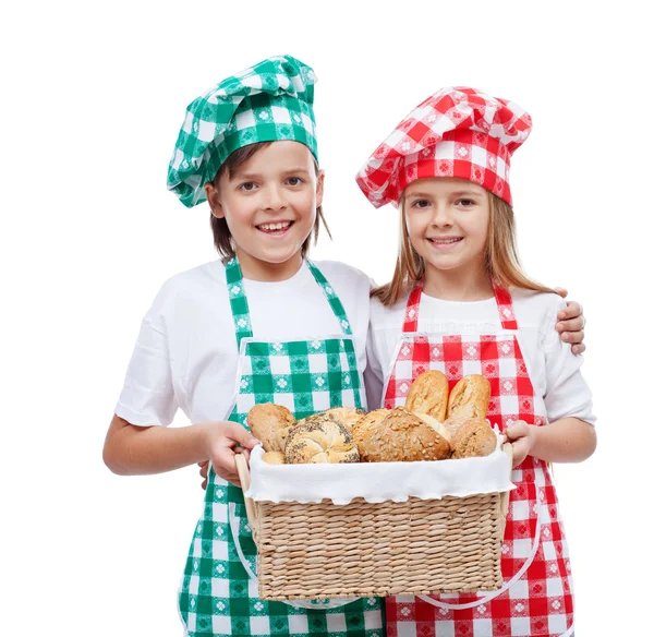 Enfants heureux avec chapeaux de chef tenant panier avec des produits de boulangerie — Photo