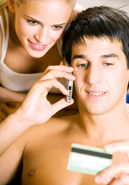 Пара с сотовым телефоном и пластиковой картой, в помещении — стоковое фото