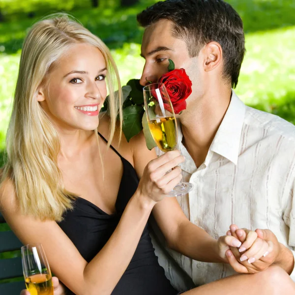 Casal jovem com presentes, rosa e champanhe, ao ar livre — Fotografia de Stock