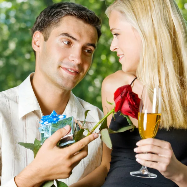 Pareja joven con regalos, rosa y champán, al aire libre — Foto de Stock