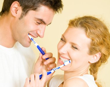 Cheerful young couple cleaning teeth together clipart