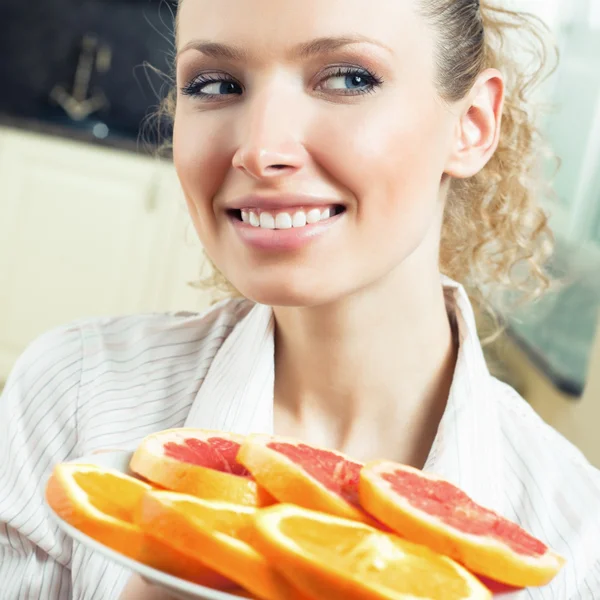 Cheerful woman with plate of oranges and grapefruit — Stock fotografie