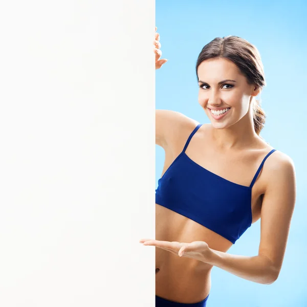 Vrouw in fitnesswear tonen uithangbord, over blauw — Stockfoto