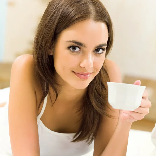 Молода щаслива усміхнена жінка п'є каву, вдома — стокове фото