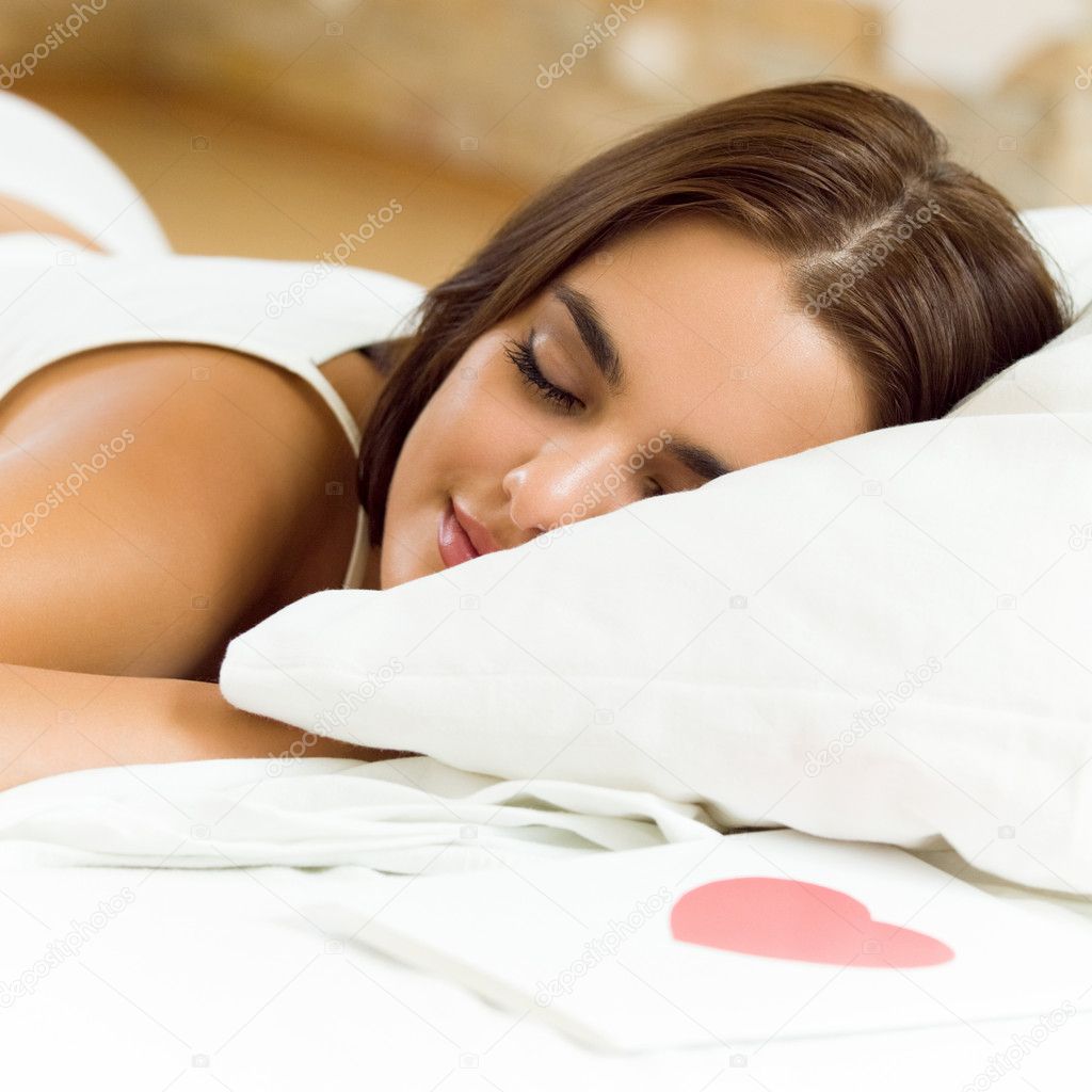 Young sleeping woman with valentine card on bed
