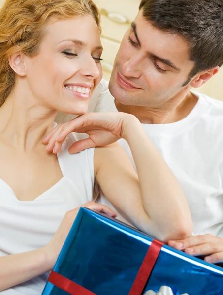 Casal amoroso alegre com presente, dentro de casa — Fotografia de Stock