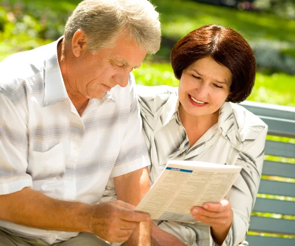 Счастливая пожилая пара читает на свежем воздухе — стоковое фото