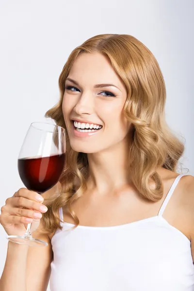 Junge glückliche Frau mit einem Glas Rotwein, auf grau Stockfoto