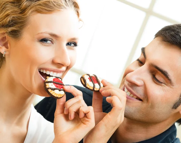 Cheerful couple eating cookies — Stock Photo, Image