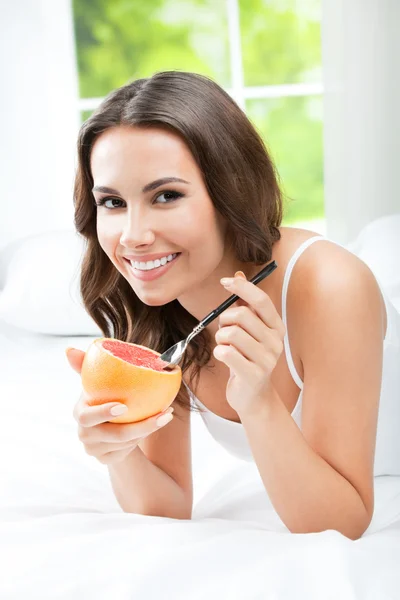 Mulher sorridente comendo toranja em casa — Fotografia de Stock