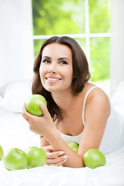 Jonge gelukkig lachende vrouw met appels, op slaapkamer — Stockfoto