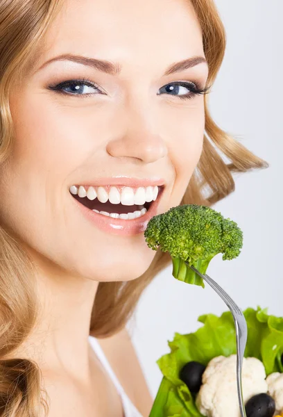 Vrouw eten broccoli, over grijs — Stockfoto