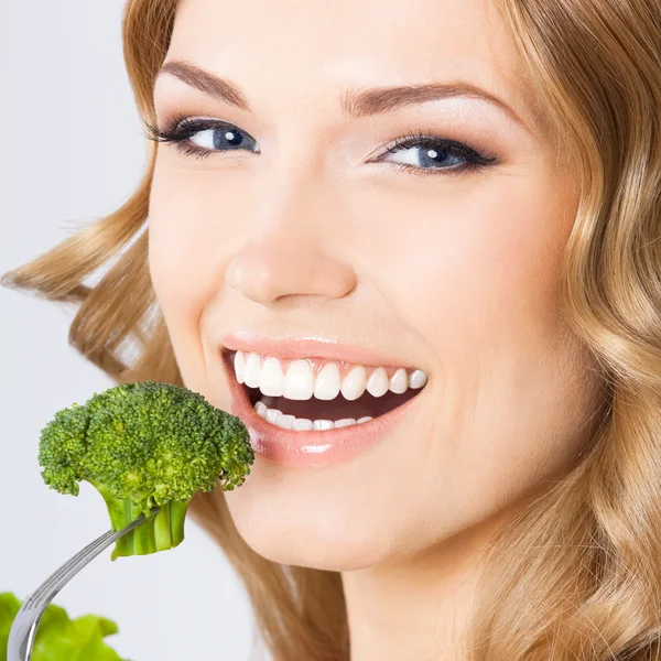 Woman eating broccoli, over gray — Stock Photo, Image