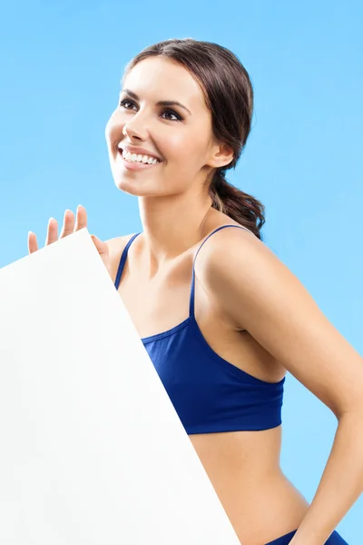 Woman in fitnesswear showing signboard, over blue — Stock Photo, Image