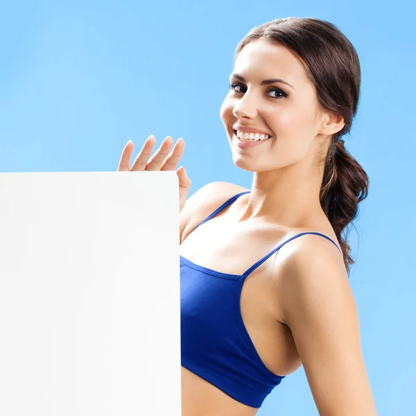 Woman in fitnesswear showing signboard, over blue — Stock Photo, Image