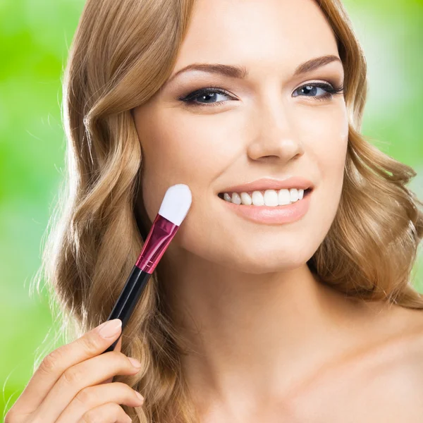 Mujer sonriente con cepillo de maquillaje, al aire libre —  Fotos de Stock