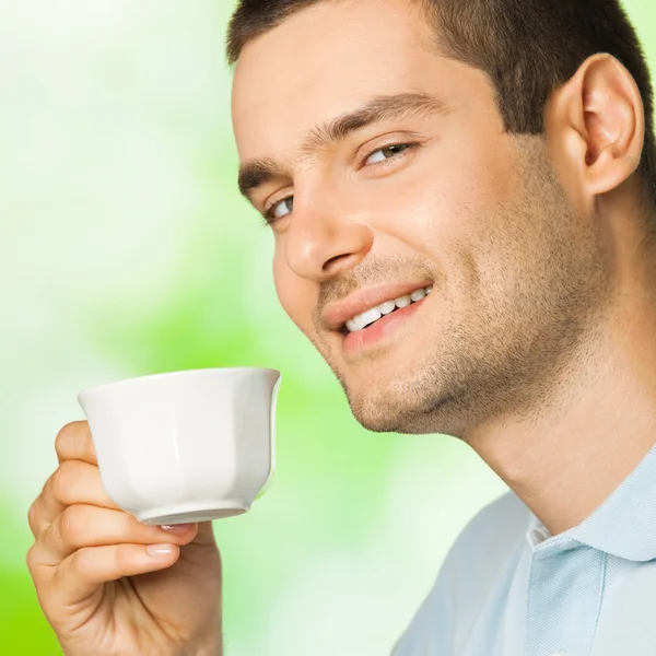 Jeune homme souriant avec une tasse de café, à l'extérieur — Photo