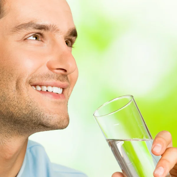 Jeune homme souriant avec verre d'eau, à l'extérieur — Photo