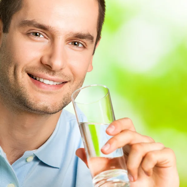 Jeune homme souriant avec verre d'eau, à l'extérieur — Photo