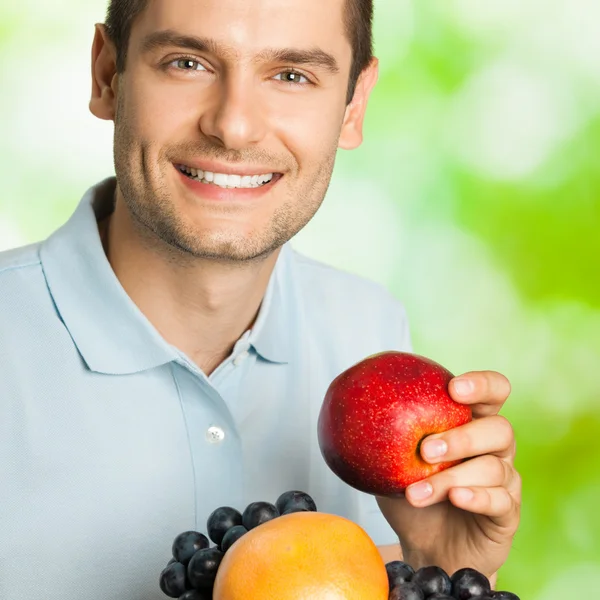 Portret van jonge gelukkig lachende man met plaat van vruchten, outdoo — Stockfoto