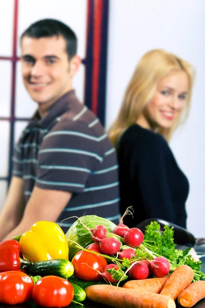 Vegetables on the table and blurred young happy smiling couple o — Stock Photo, Image