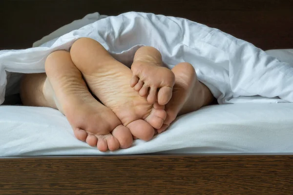 Legs of man and woman lying on bed under duvet
