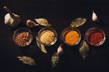 Sarımsak, defne yaprağı ve karabiberli koyu bir zemin üzerinde farklı baharatlar.