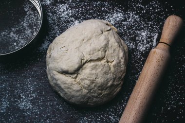 Pizza dough with rolling pin and sieve on wooden table, dough ball and wooden rolling pin and sieve on dark background