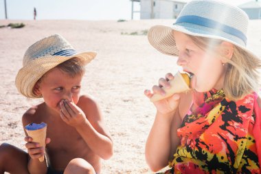 Havada dinlenen sarışın bir oğlan ve şapkalı sarışın bir kız kumsalda, kumsalda oturuyor ve dondurma yiyor ya da tadıyor küçük bir tarla derinliği ve kopyalama alanı ile. Tatil kavramı  