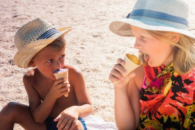 Havada dinlenen sarışın bir oğlan ve şapkalı sarışın bir kız kumsalda, kumsalda oturuyor ve dondurma yiyor ya da tadıyor küçük bir tarla derinliği ve kopyalama alanı ile. Tatil kavramı  