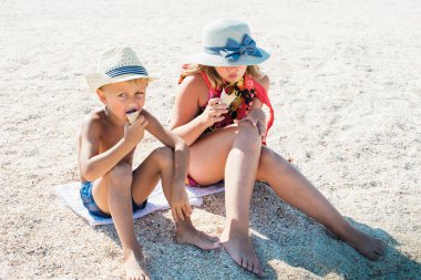 Havada dinlenen sarışın bir oğlan ve şapkalı sarışın bir kız kumsalda, kumsalda oturuyor ve dondurma yiyor ya da tadıyor küçük bir tarla derinliği ve kopyalama alanı ile. Tatil kavramı  