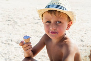 Hasır şapkalı beyaz sarışın bir çocuk kumsalda oturur, kumdaki dondurmayı yer ya da yalar ve alanı kopyalardı. Dinlenme, rahatlama, çocuk