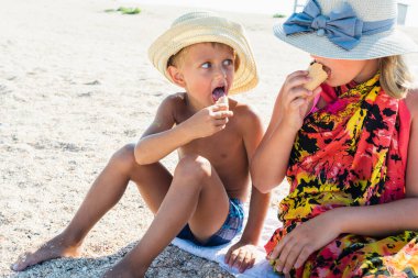 Havada dinlenen sarışın bir oğlan ve şapkalı sarışın bir kız kumsalda, kumsalda oturuyor ve dondurma yiyor ya da tadıyor küçük bir tarla derinliği ve kopyalama alanı ile. Tatil kavramı  