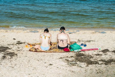 Bikini giymiş, sırtı denize dönük oturan bir kız. Denize bakmak, açık hava aktiviteleri, tatil