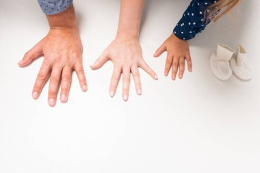 Baba, anne, kız ve küçük çorapların elleri parlak, genç beyaz bir aile ikinci çocuklarının doğmasını bekliyor. Mutlu aile kavramı. Bekleyen bebek, beyaz arka planda izole edilmiş eller. 