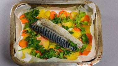 Fırında pişirmeden önce sebzeli, patatesli, havuçlu taze moraine uskumrusu, metal bir şekilde. Sebzeli balık. Gri arkaplan, üst manzara. Ev yemekleri..